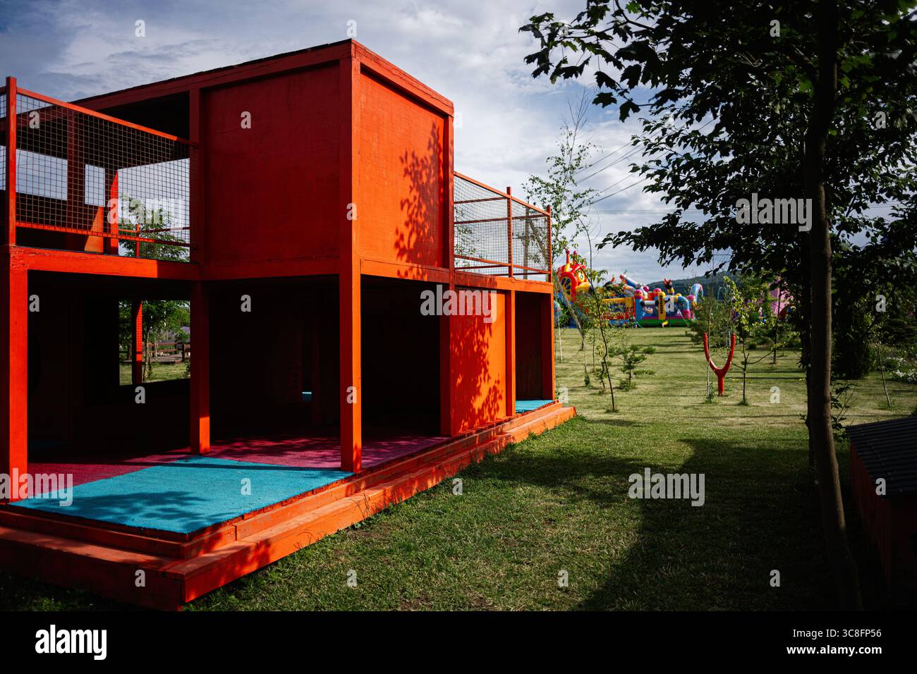 Lebendig roter Spielbereich mit farbenfrohen Details, umgeben von üppigem Gras und Bäumen. Stockfoto Lebendig roter Spielbereich mit farbenfrohen Details, umgeben von üppigem Gras und Bäumen. Stockfoto