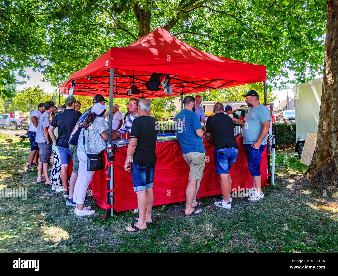 Gruppe von Menschen, die am heißen Sommertag im Bierzelt unter Schatten der Bäume trinken - Paulmy, Indre-et-Loire (37), Frankreich. Stockfoto