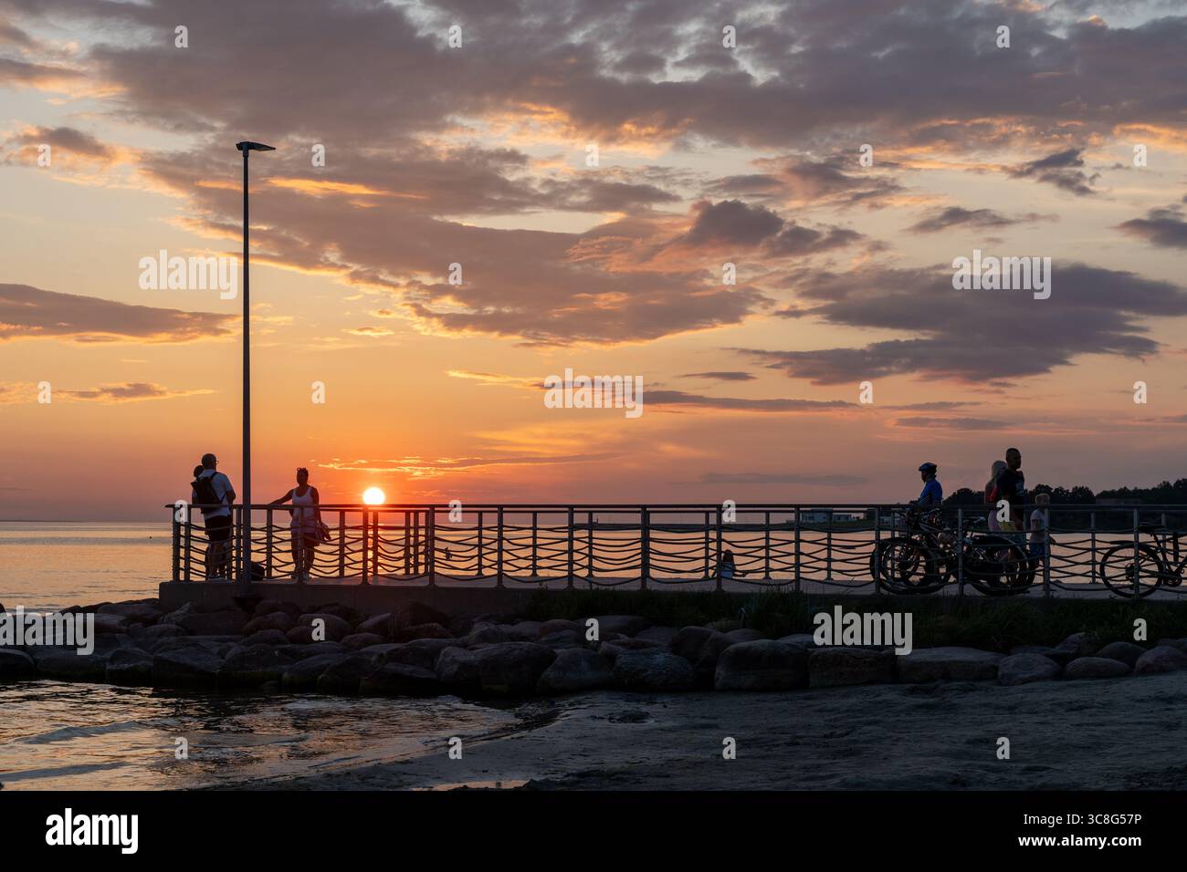 Menschen, die den Sonnenuntergang auf der Viimsi Promenade beobachten, mit Radfahrern, die sich gegen den Golf von Finnland, Estland, abspielen Stockfoto