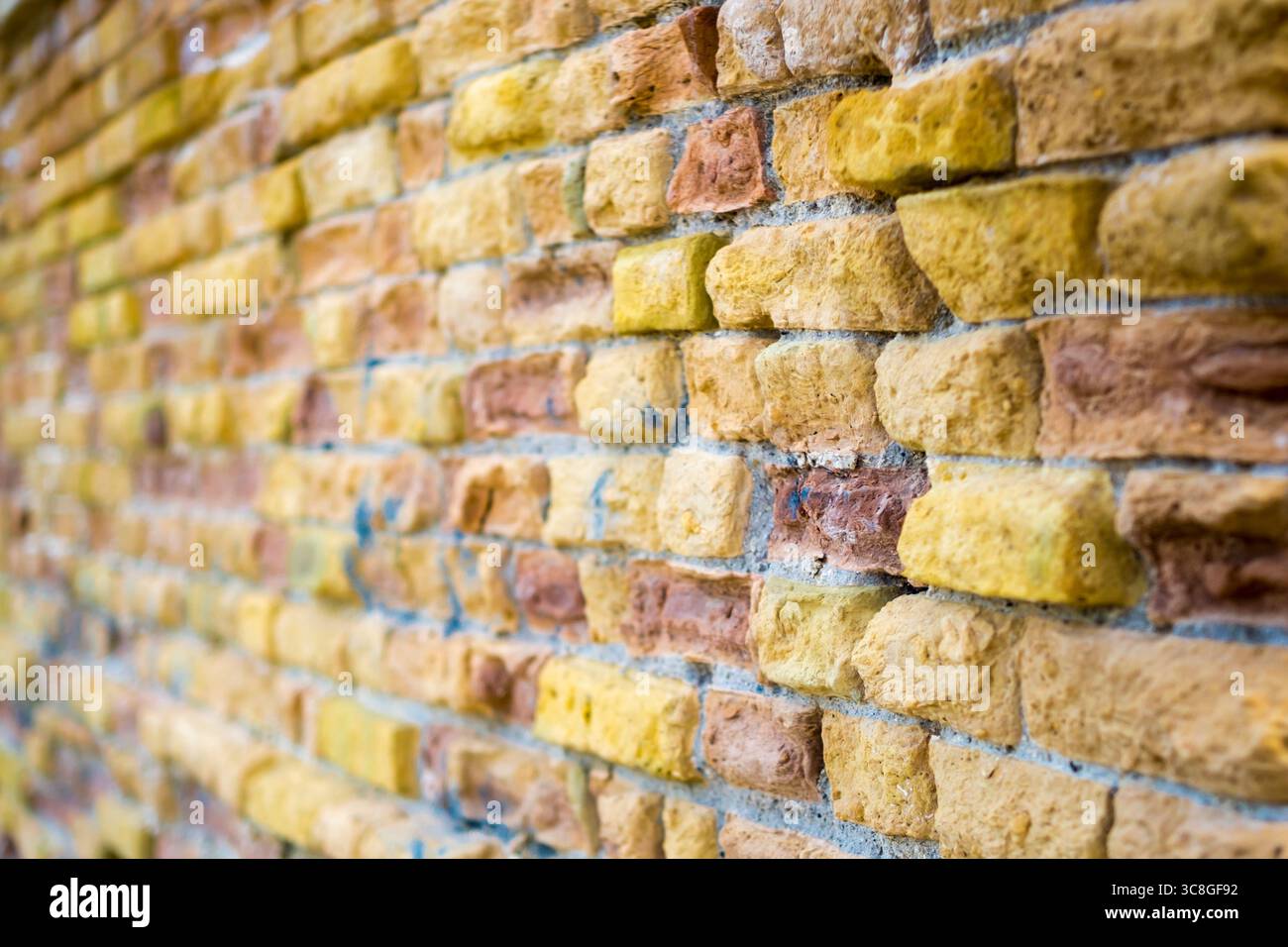 Verwitterte Ziegelwand in Gelb- und Orangetönen, die komplizierte Oberflächendetails aus nächster Nähe offenbaren Stockfoto