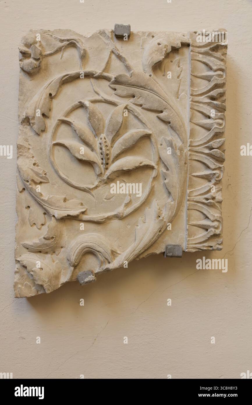 Eine Basreliefskulptur, die eine stilisierte Vase darstellt, umgeben von kunstvollen dekorativen Elementen. Das Relief ist mit komplizierten Blumenmotiven und einem drapierten Dekor versehen Stockfoto
