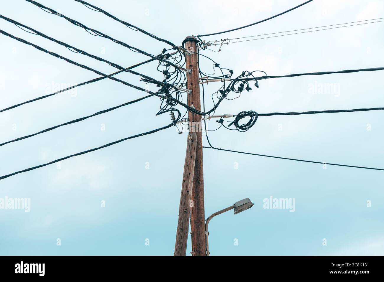 Nahaufnahme eines hölzernen Versorgungsmasts mit verwickelten elektrischen Kabeln gegen einen hellen Himmel. Selektiver Fokus. Stockfoto