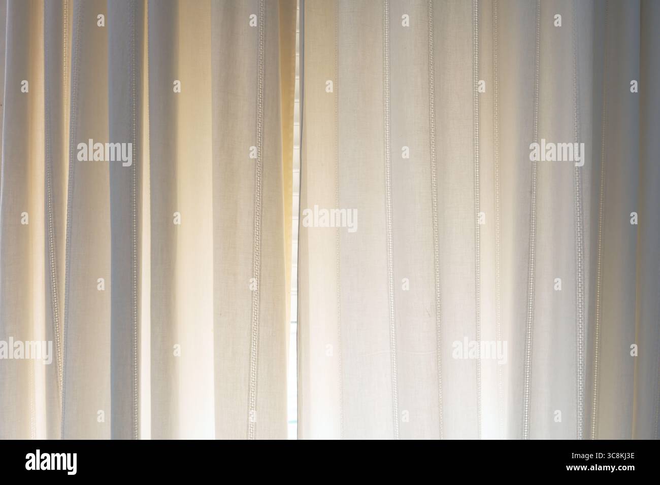 Transparente beigefarbene Vorhänge mit vertikalen Nähten, die von natürlichem Tageslicht sanft beleuchtet werden. Minimalistische Inneneinrichtung in beruhigenden, warmen Tönen. Abstra Stockfoto