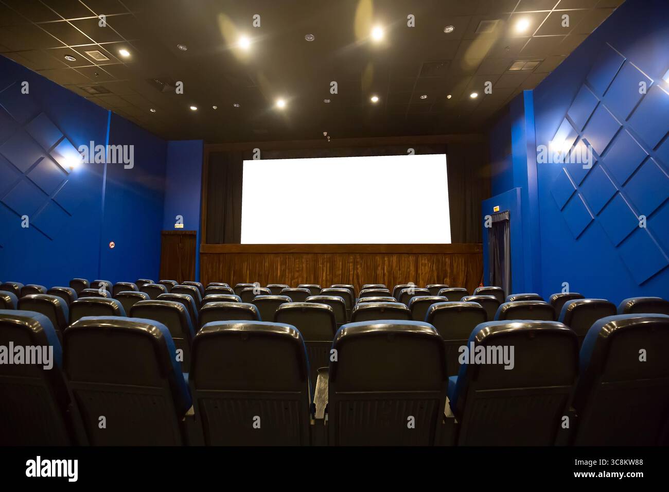 Leerer Kinosaal mit leerem weißen Bildschirm. Leere Reihen blauer Theater- oder Filmsitze. Stockfoto