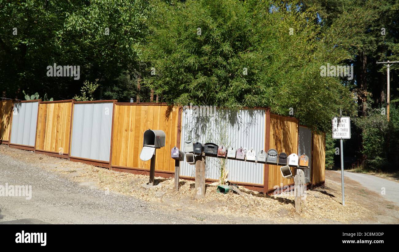 Eine Reihe von ländlichen Briefkästen steht am Eingang zu einer privaten Fahrt in Nordkalifornien, mit einem Holz- und Metallzaun im Hintergrund Stockfoto