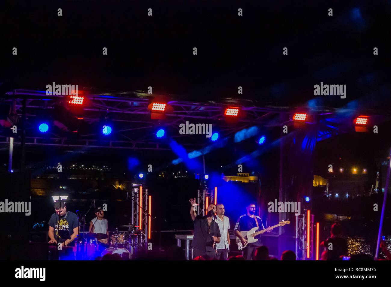Nächtliche Konzertaufführung mit Band auf der Bühne im Freien, beleuchtet von bunten Lichtern Stockfoto