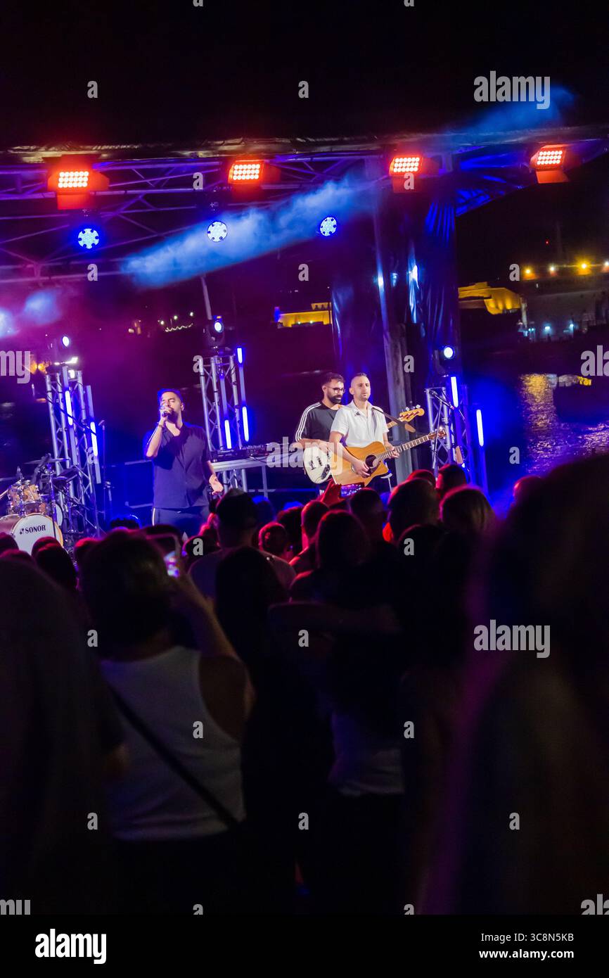Nächtliche Konzertaufführung mit Band auf der Bühne im Freien, beleuchtet von bunten Lichtern Stockfoto