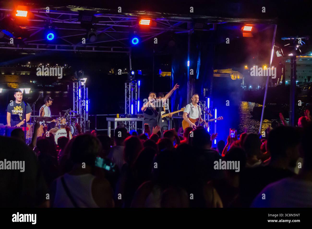Nächtliche Konzertaufführung mit Band auf der Bühne im Freien, beleuchtet von bunten Lichtern Stockfoto