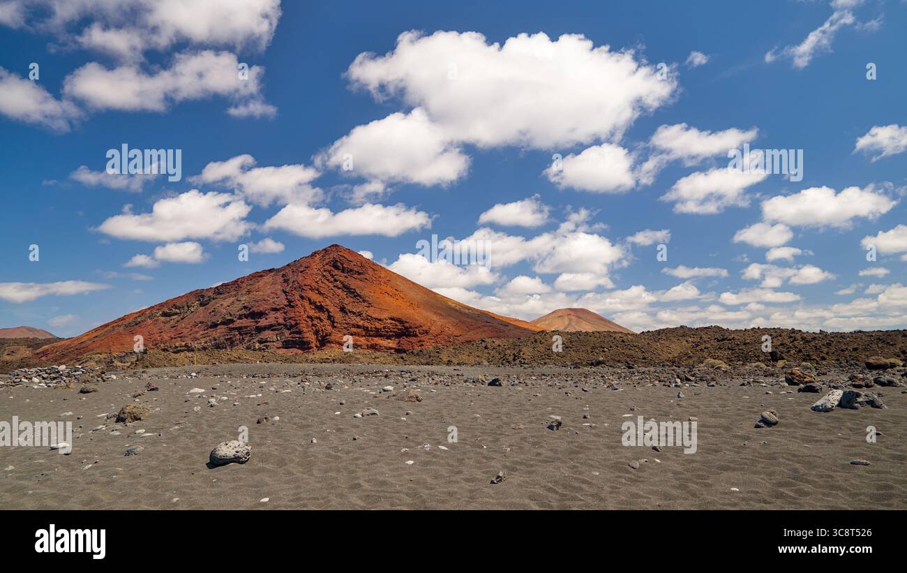 Wunderschöne Lanzarote Landschaft mit einem erloschenen Vulkan im Hintergrund unter einem blauen Himmel voller flauschiger Schafwolken. Stockfoto