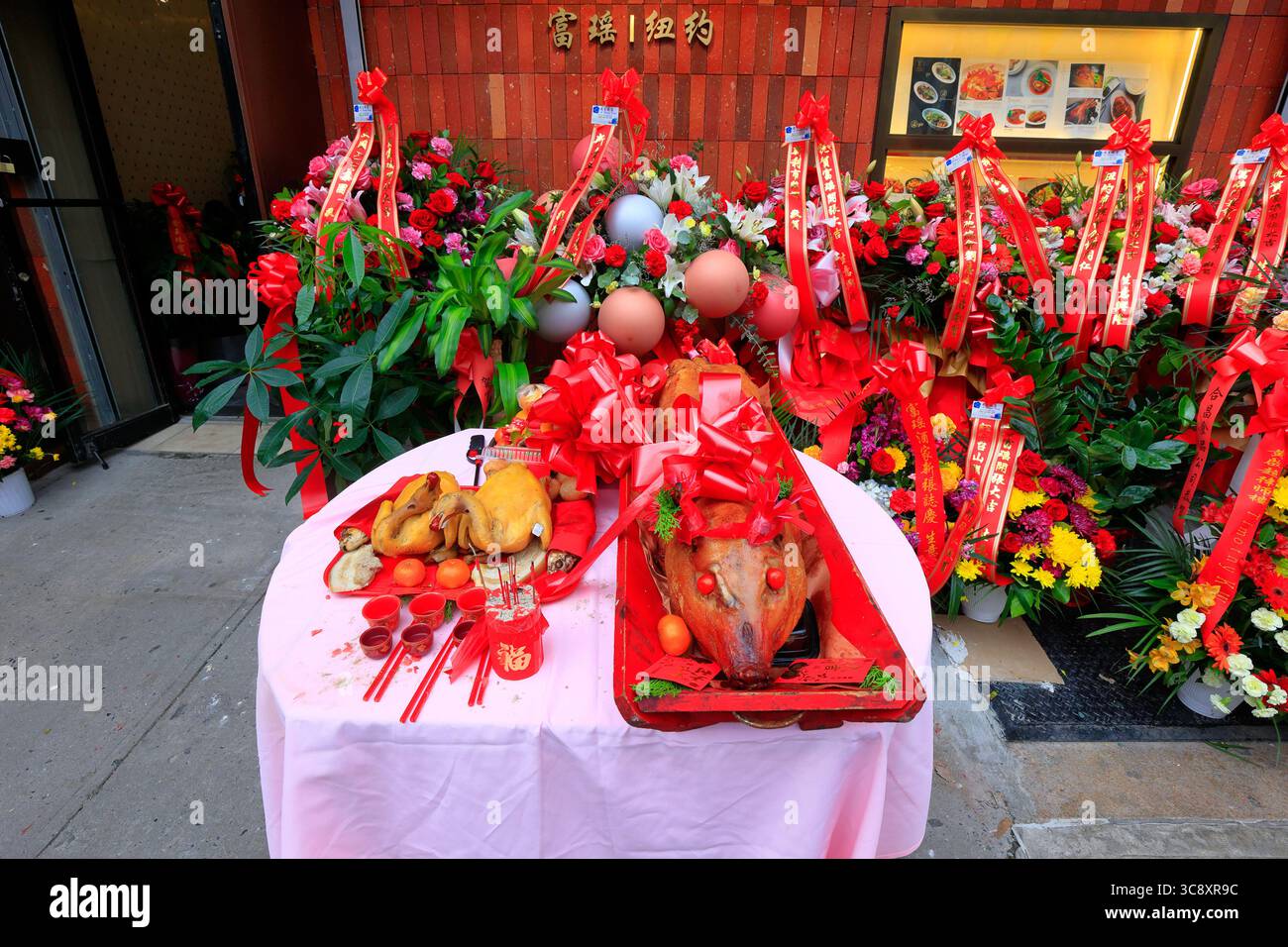 Rote Blumenkörbe und eine Zeremonie zum Schneiden von Schweinebraten zur großen Eröffnung eines chinesischen Restaurants. 大吉大利 燒豬 客似雲來 拜神 Stockfoto