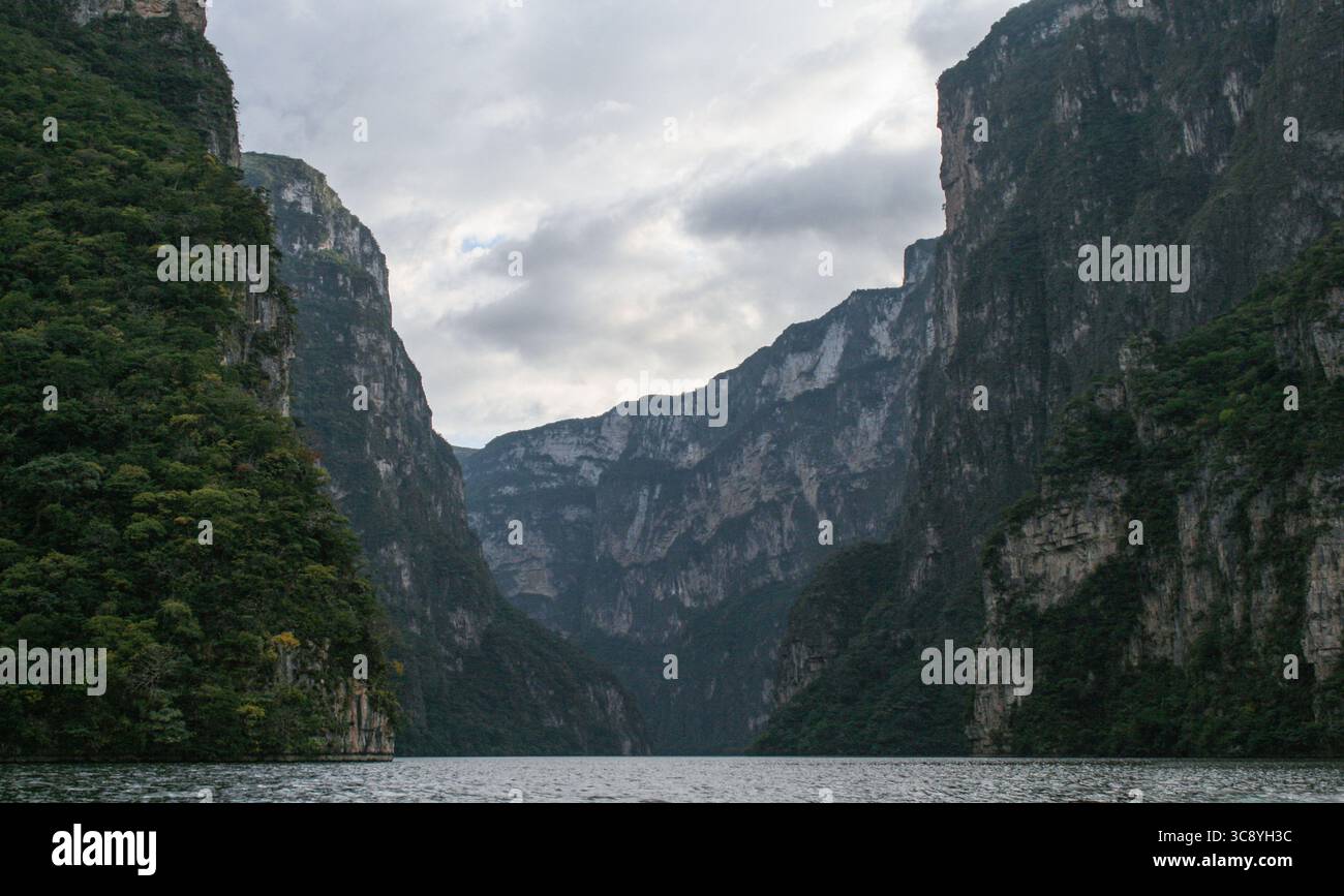 Sumidero Canyon unter bewölktem Himmel in Chiapas, Mexiko. Der Fluss Grijalva fließt leise zwischen hoch aufragenden Kalksteinklippen, die in tiefgrünes Gemüse gehüllt sind Stockfoto