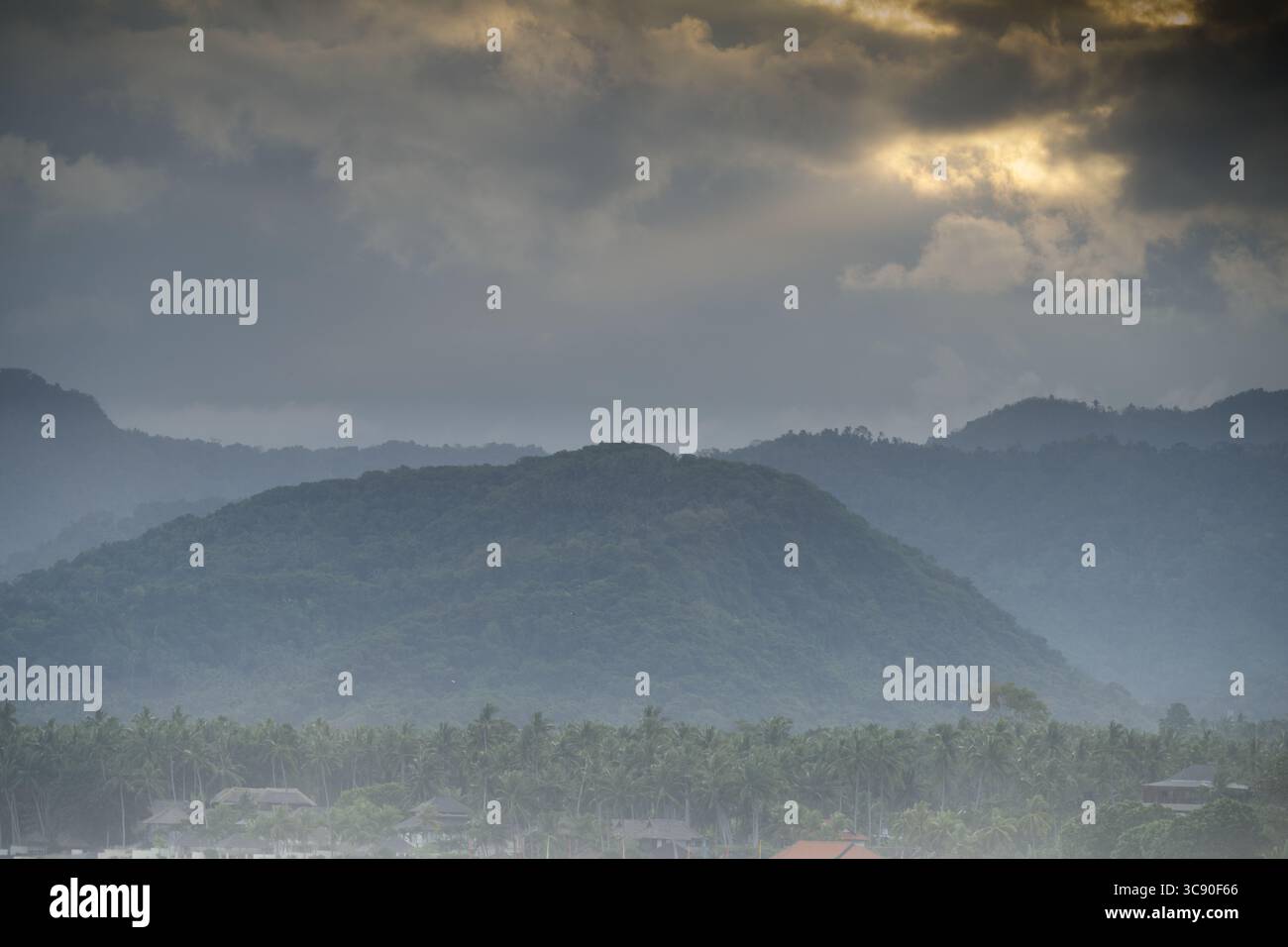 Eine ruhige Landschaft auf Bali entfaltet sich unter einem stimmungsvollen, bewölkten Himmel. Das Bild zeigt mehrere Schichten bewaldeter Hügel, die langsam in die Ferne versinken. Stockfoto