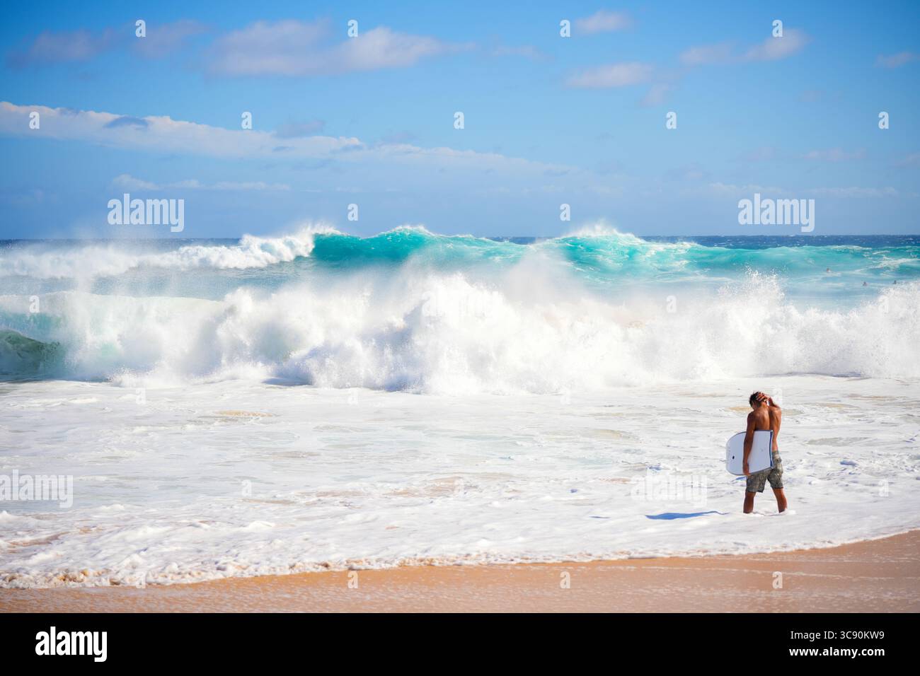 Bodyboarder sehen sich unter hellem Himmel mit der aufragenden blauen Welle konfrontiert, die den Nervenkitzel und die Energie extremer Meeressportarten in kristallklarer Brandung einfängt Stockfoto