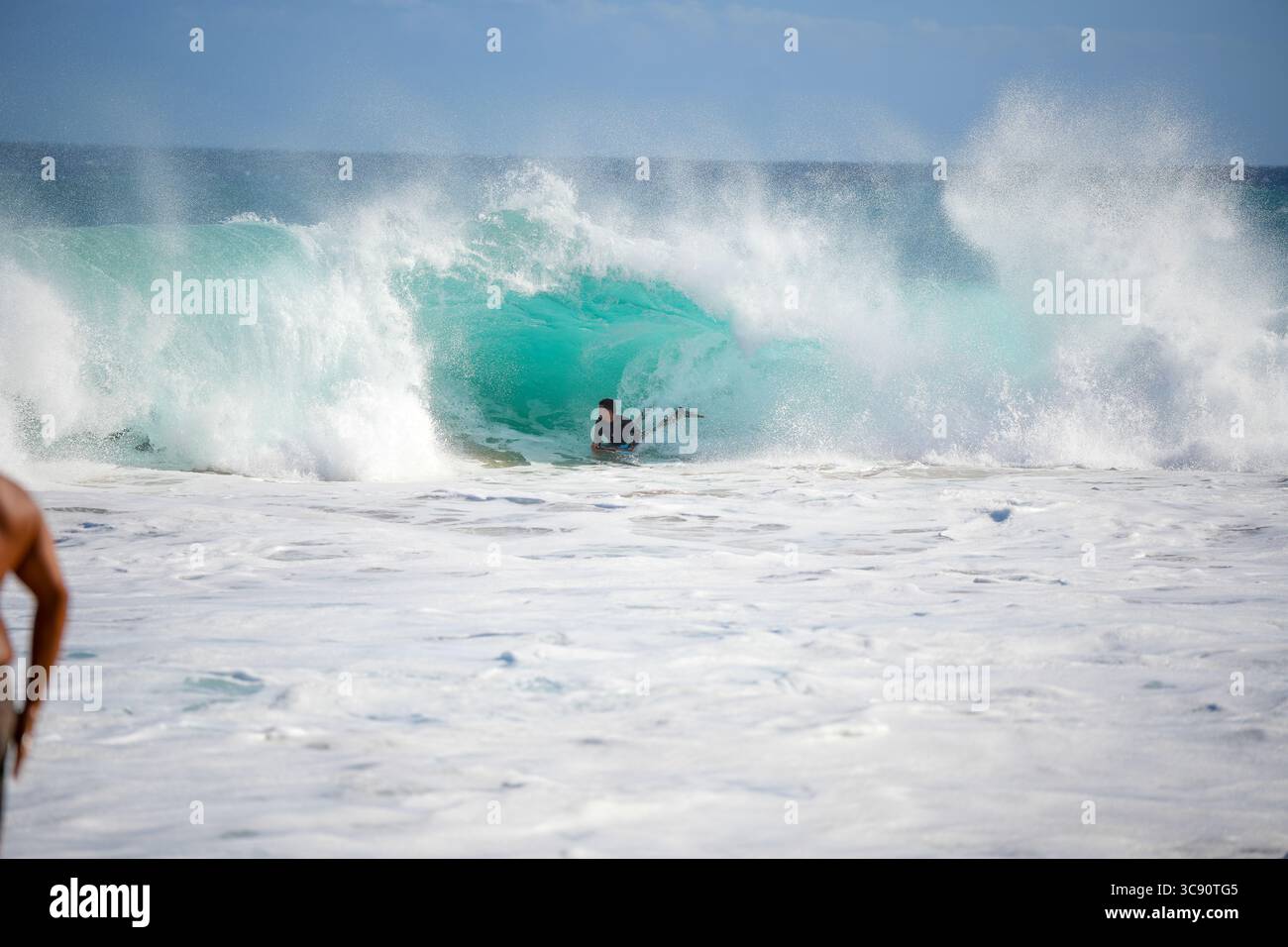 Bodyboarder reitet in einem gewaltigen Sturmschwall, der sich mit Kraft und Präzision vor dem Hintergrund des turbulenten Ozeanhimmels durch schäumende Wellen zieht. Honolulu HI Stockfoto