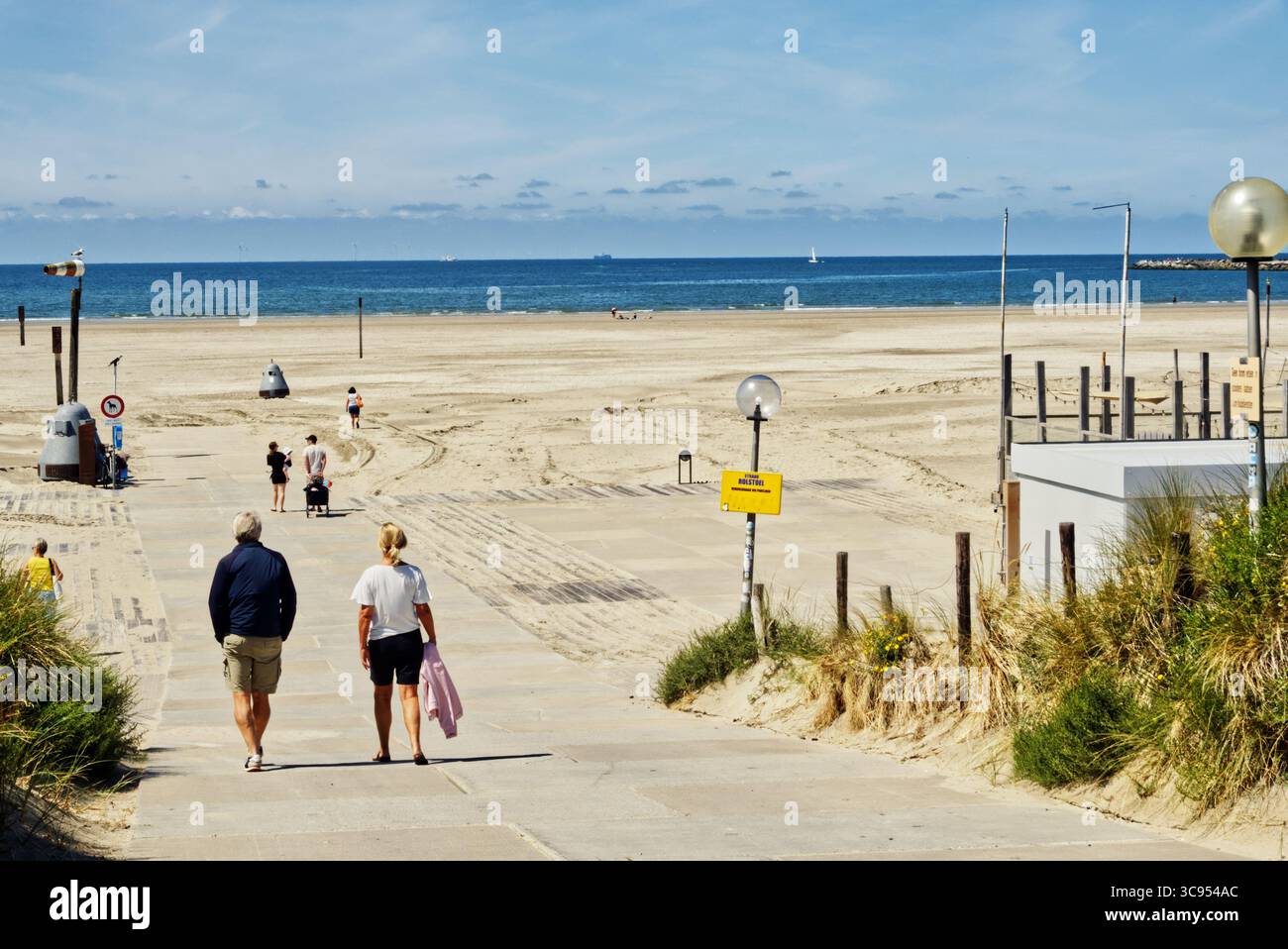 Reife Partner schlendern durch die Sandküste, tragen legere Sommerkleidung und genießen die Nordseelandschaft unter hellem Sonnenlicht Stockfoto