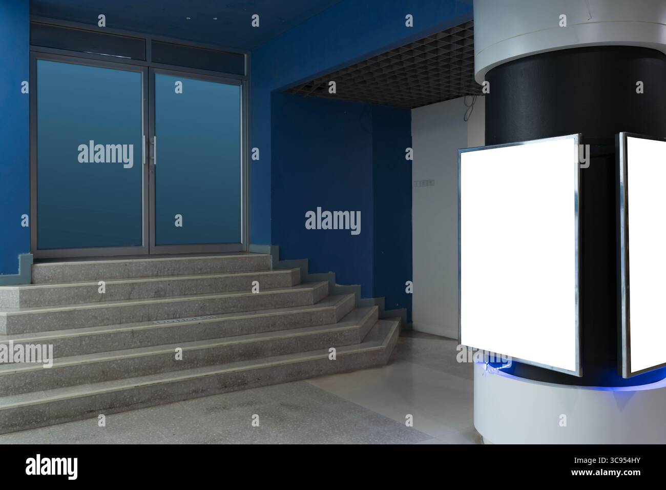 Eine leere beleuchtete Werbe-Lichtbox steht im modernen Innenraum in der Nähe einer Treppe und einer geschlossenen Glastür. Geeignet für kommerzielles Design, Digital Signage, Stockfoto