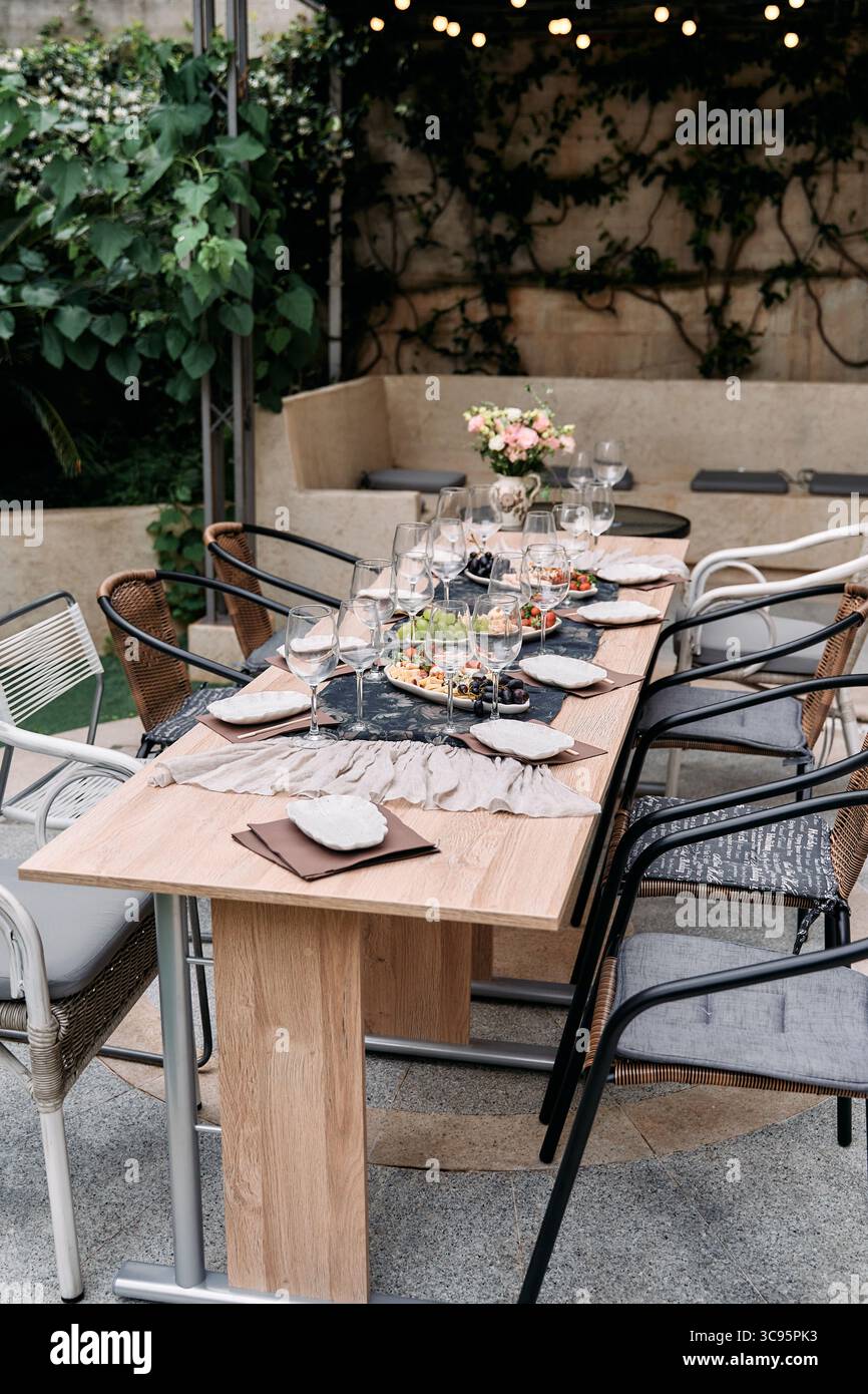 Elegantes Esstisch-Set im Freien für ein unvergessliches Treffen umgeben von üppigem Grün und warmer Atmosphäre, ideal für kleine Feiern oder Familien-DIN Stockfoto