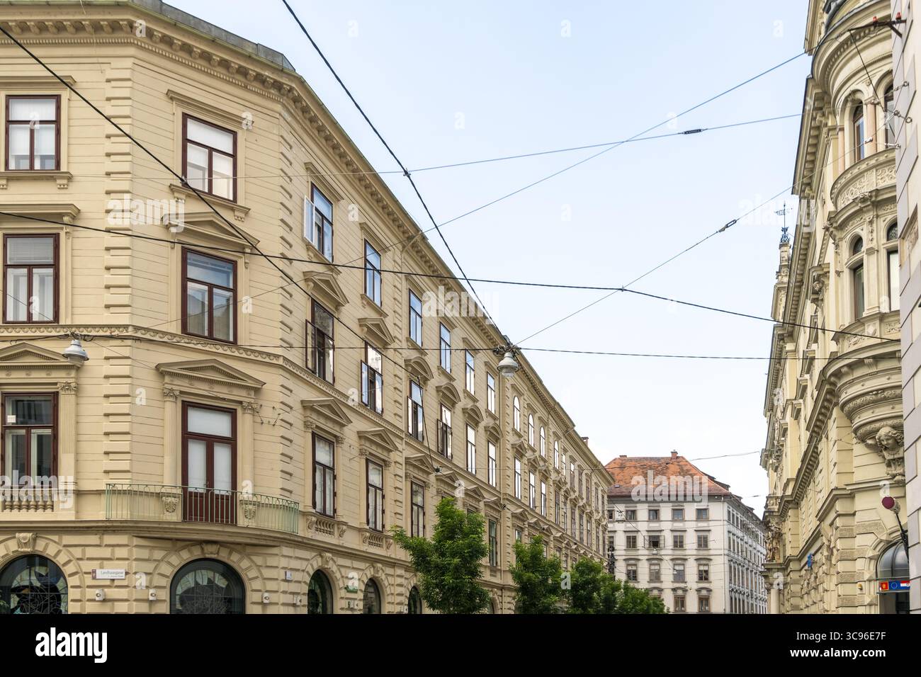 Der Blick auf verzierte, beigefarbene Gebäude erhebt sich vor einem weichen Himmel, durchzogen von dünnen schwarzen Drähten, die auf die pulsierende Energie der Stadt hinweisen, Graz, Österreich. Stockfoto