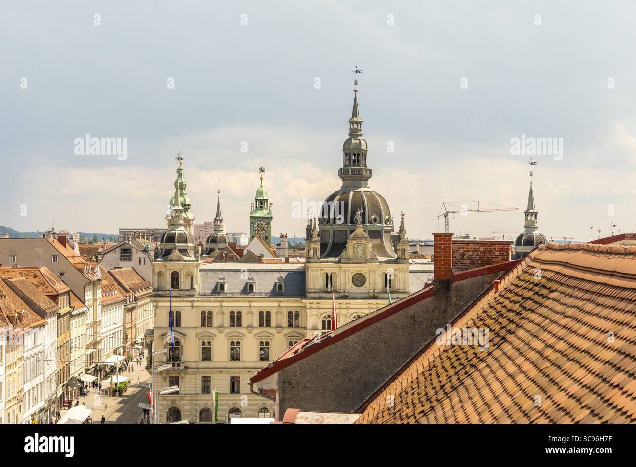 Blick auf das Rathausgebäude mit verzierten Türmen und einer dunklen Kuppel, die sich über Terrakottadächern unter hellem Himmel erhebt, Graz, Steiermark, Österreich. Stockfoto