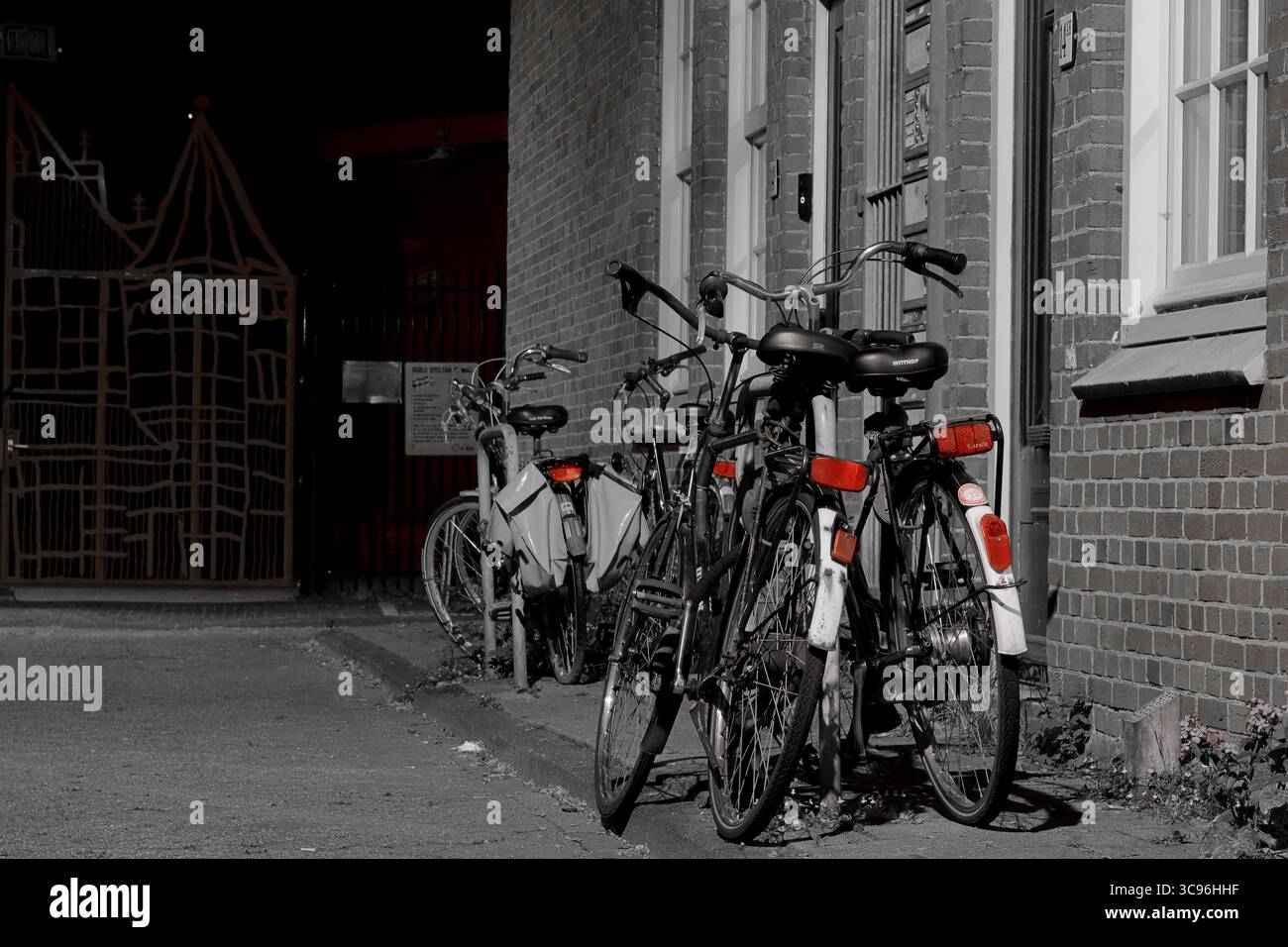 Eine Reihe von Fahrrädern, die nachts an einer Ziegelfassade auf einer Amsterdamer Straße geparkt sind, mit warmem Licht und Schatten, perfekt für urbane Kunstdrucke. Stockfoto