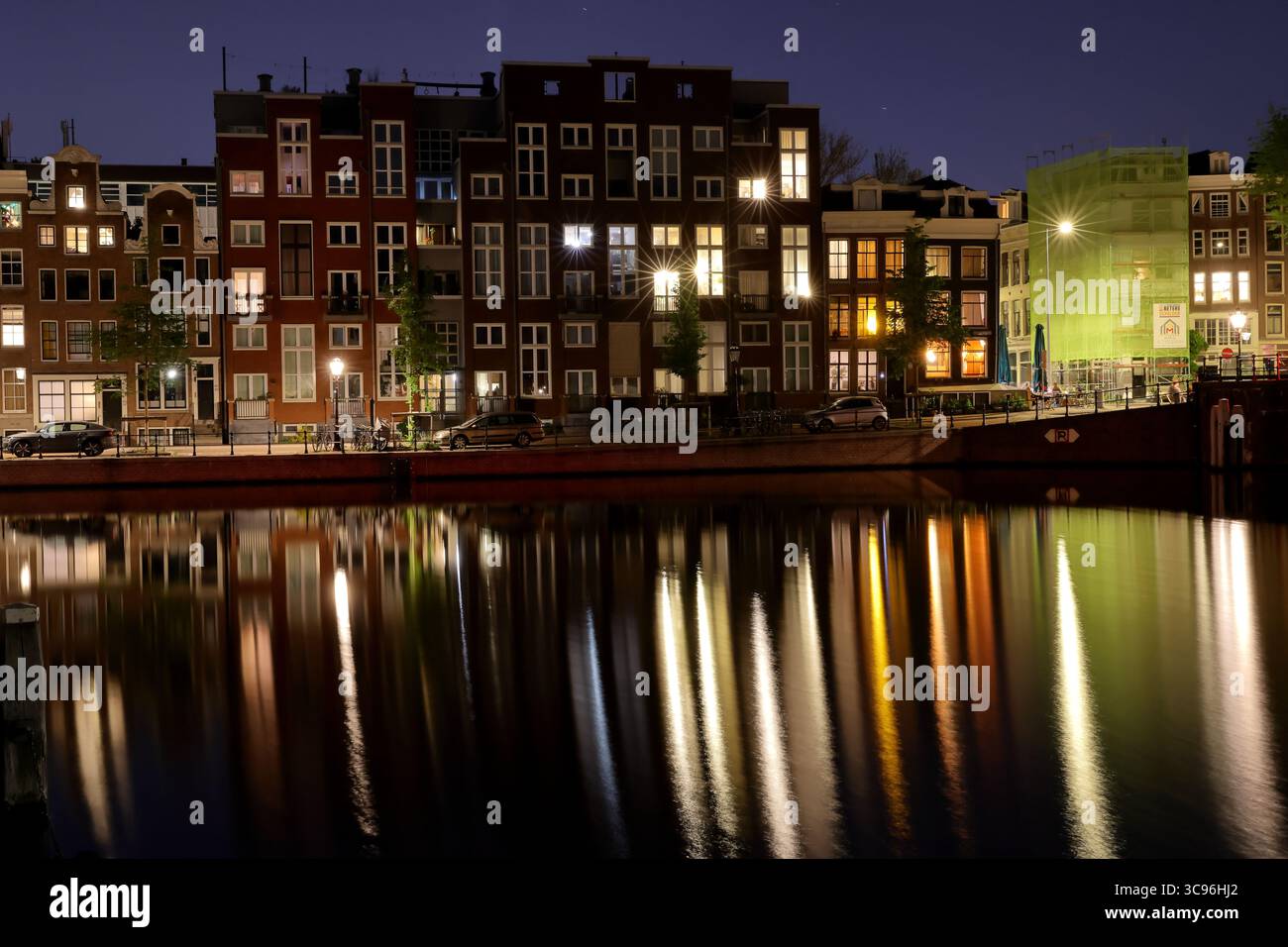 Historische Grachtenhäuser und beleuchtete Bäume schimmern im Amsterdamer Entrepotdok, während die lange Exposition die Nachtschichten und das urbane Ambiente am Wasser einfängt. Stockfoto