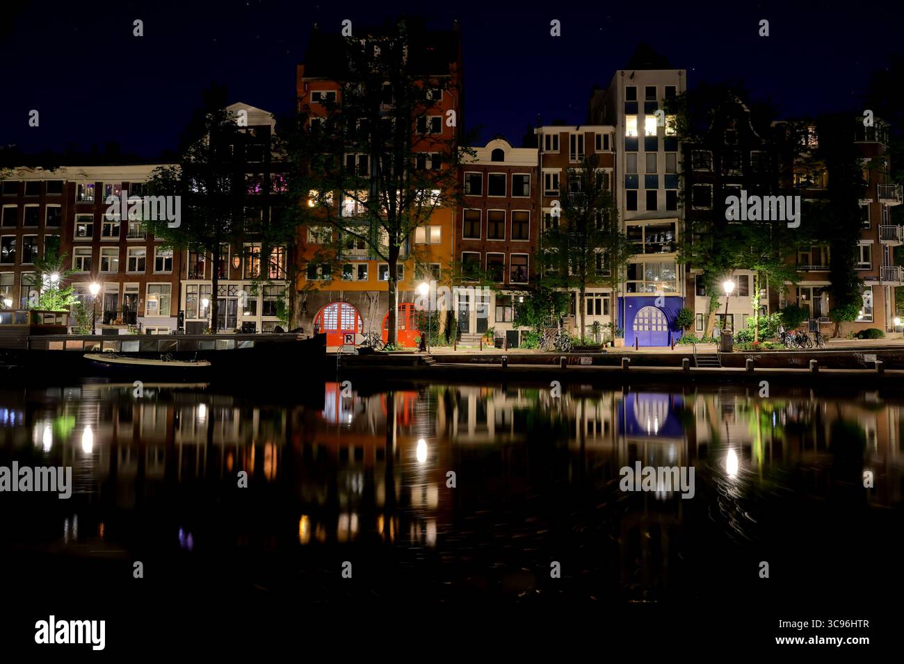 Funkelnde Lichter der Stadt tanzen auf dem ruhigen Wasser des Zwanenburgwal-Kanals in Amsterdam und spiegeln historische Fassaden in einem ruhigen nächtlichen Panorama wider. Stockfoto