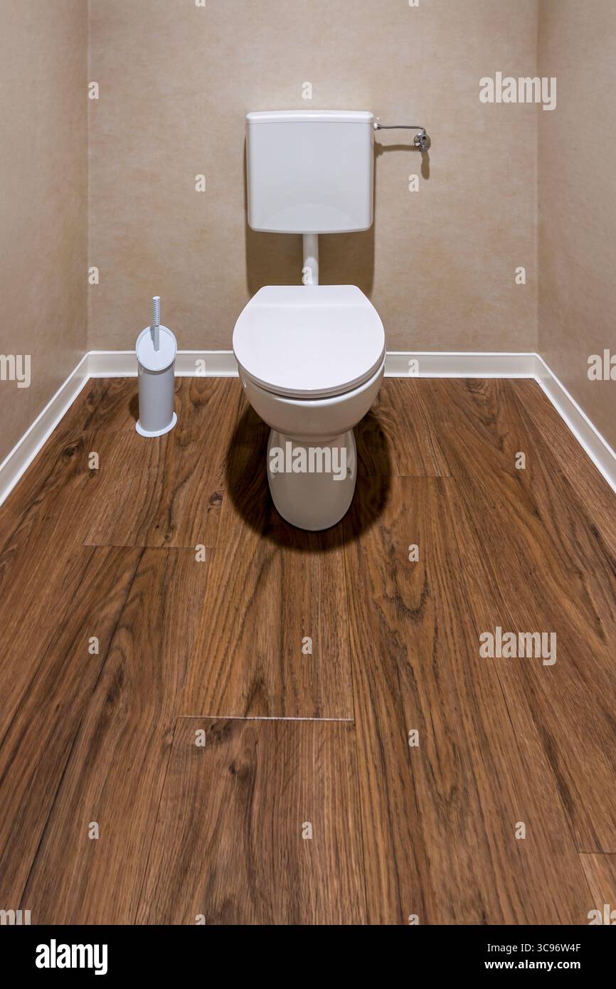 Weiße Toilettenschüssel mit geschlossenem Deckel und Spültank und Bürstenhalter an brauner Wand und Holzboden, minimaler Aufbau mit Kopierraum Stockfoto