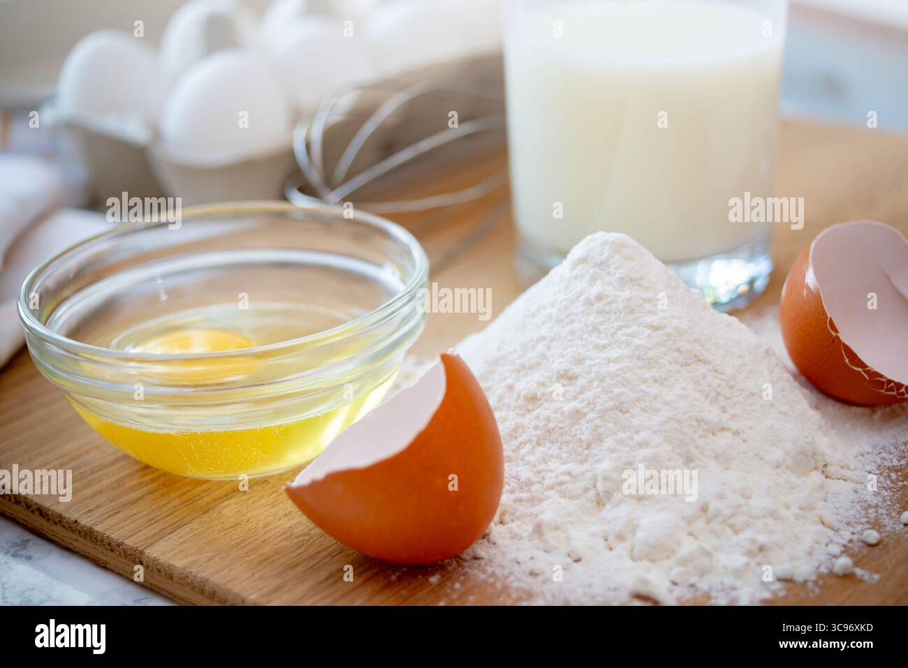 Mehl wird auf einem Holzbrett zusammen mit zerrissenen Eiern und einem Glas Milch aufgehäuft, bereit für Backzubereitungen in der Küche. Stockfoto