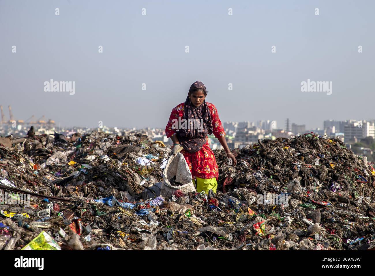 Chittagong, Bangladesch - 08. März 2024: Blick auf eine Frau inmitten der weitläufigen, strukturierten Landschaft der Deponie Sholoshohor im Kontrast zum Himmel der Stadt Stockfoto