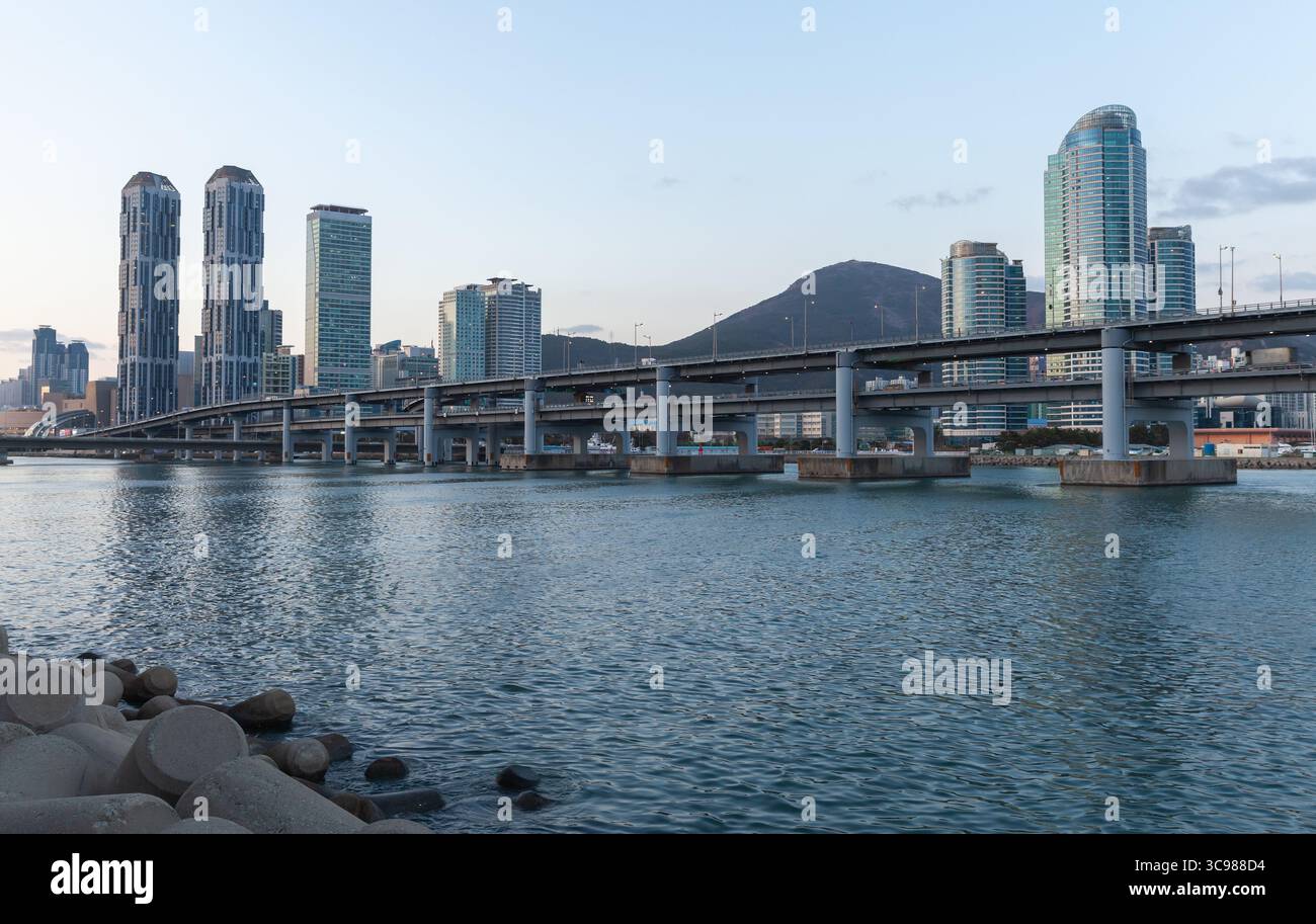 Busan, Südkorea. Blick auf die Stadt mit einer modernen Brücke über blaues Wasser mit modernen Wolkenkratzern und einem fernen Berg unter einem klaren s Stockfoto