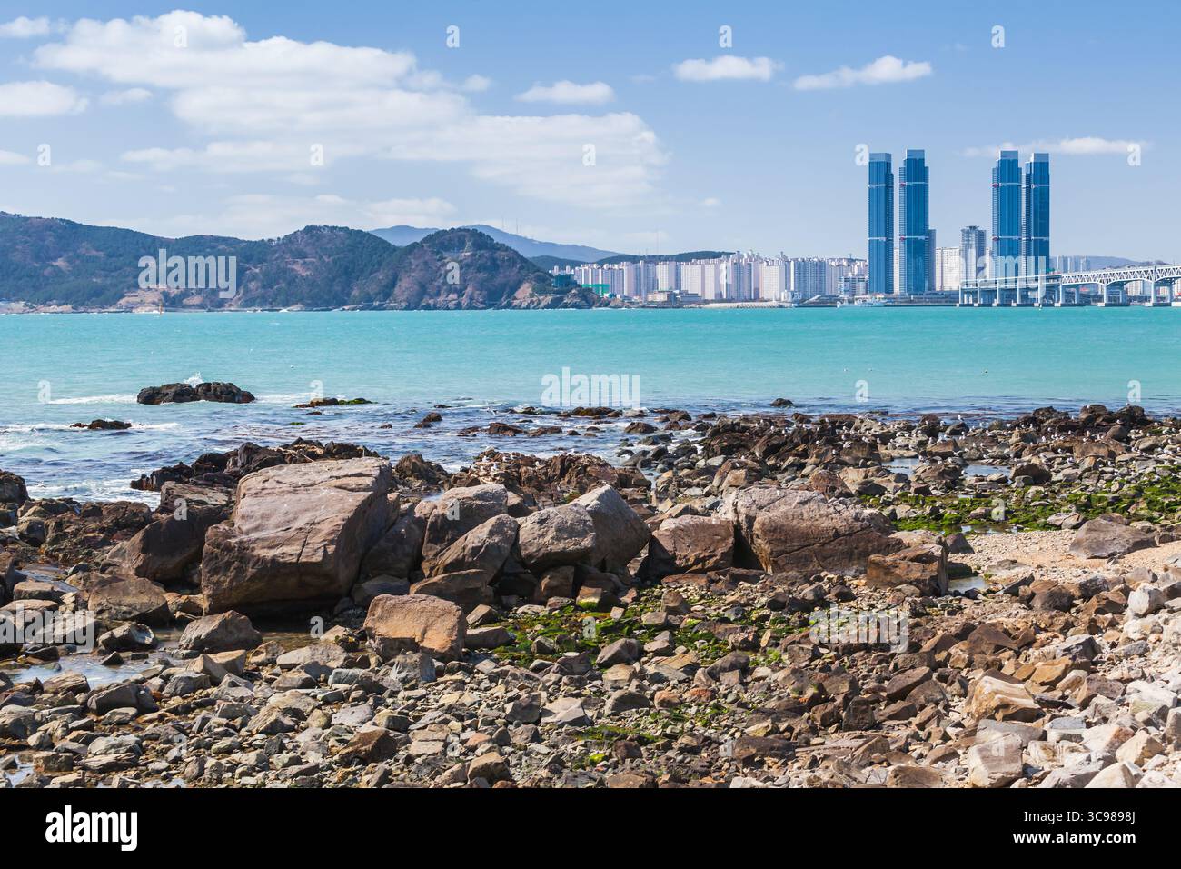 Eine lebhafte Küstenstadt von Busan mit hohen modernen Gebäuden, türkisfarbenem Wasser und einer felsigen Küste an einem hellen sonnigen Tag. Südkorea Stockfoto