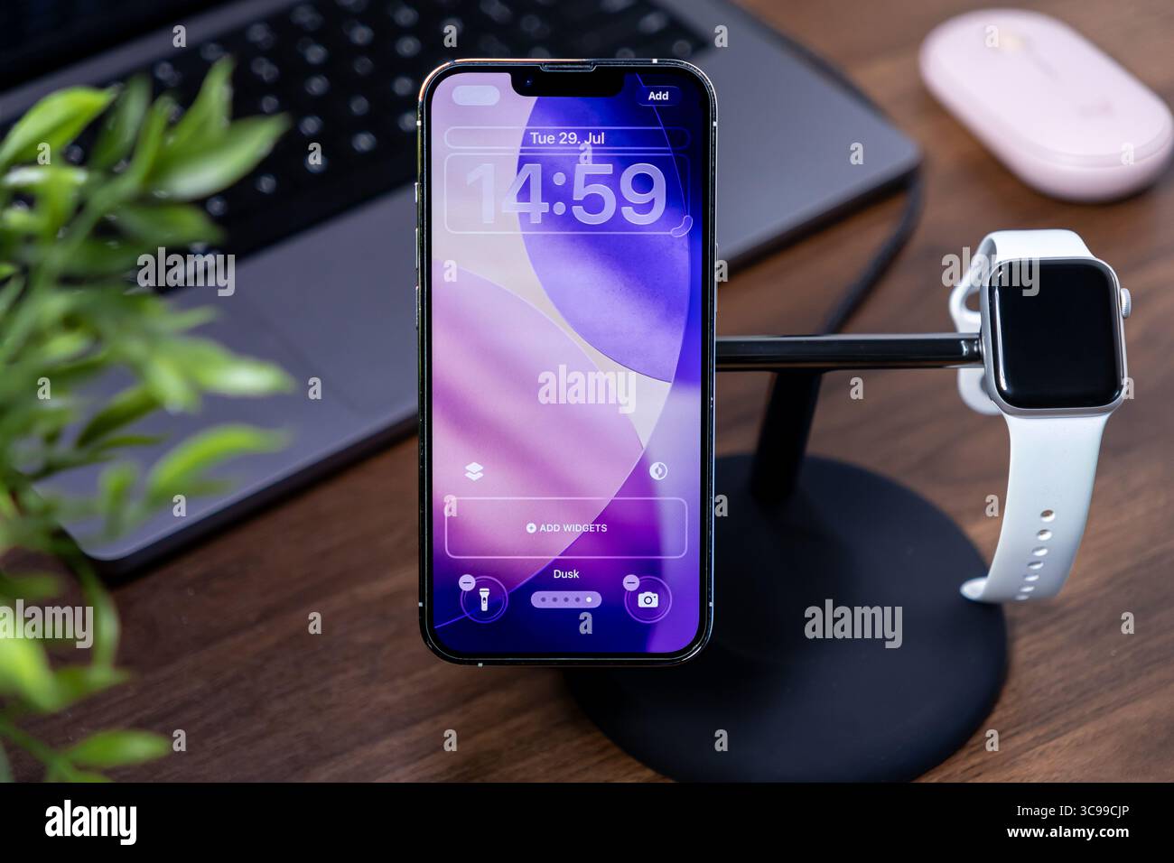 Posen, Polen - 29. Juli 2025: Modernes Smartphone auf Ladestation, zeigt ios 26-Sperrbildschirm mit abstraktem Flüssigglashintergrund, für digitale Verbindung Stockfoto