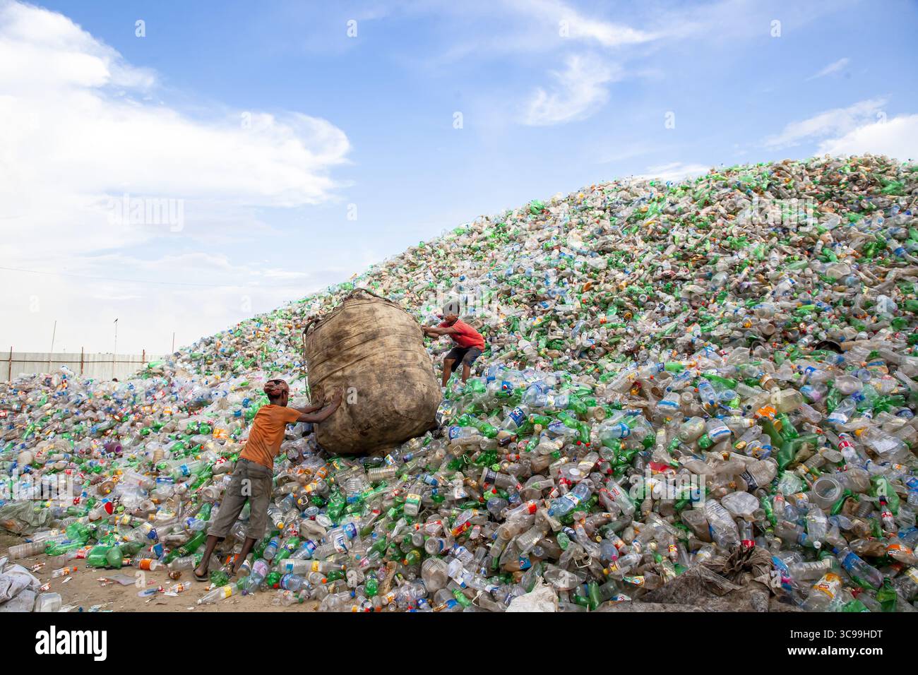 Chittagong, Bangladesch - 22. September 2022: Blick auf zwei Jungen, die einen großen Sack inmitten eines riesigen, hoch aufragenden Berges aus weggeworfenen Plastikflaschen bewegen. Stockfoto
