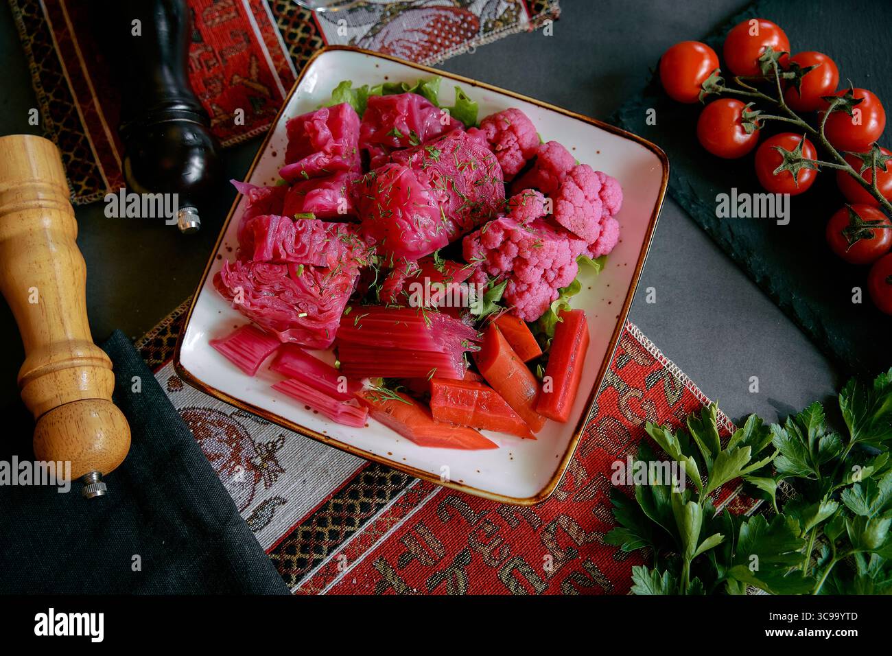Ein lebhaftes Gericht mit frisch zubereitetem rosafarbenem Blumenkohl, Rotkohl und bunten Karotten, garniert mit Kräutern und saftiger Kirschtomate Stockfoto