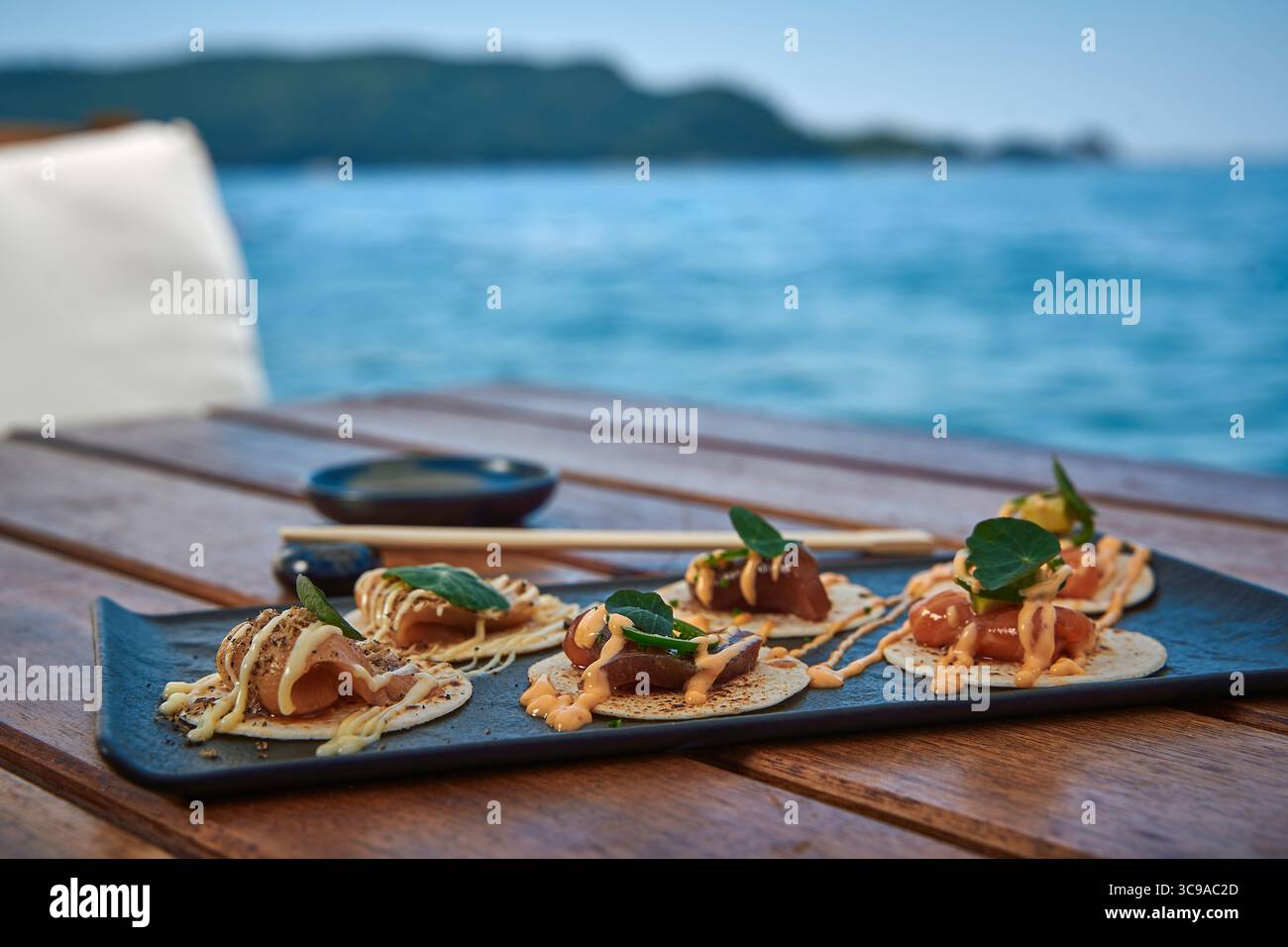 Ein wunderschön gestalteter Tacos mit Gourmet-Meeresfrüchten und frischen Zutaten, serviert auf einem Holztisch am Meer Stockfoto