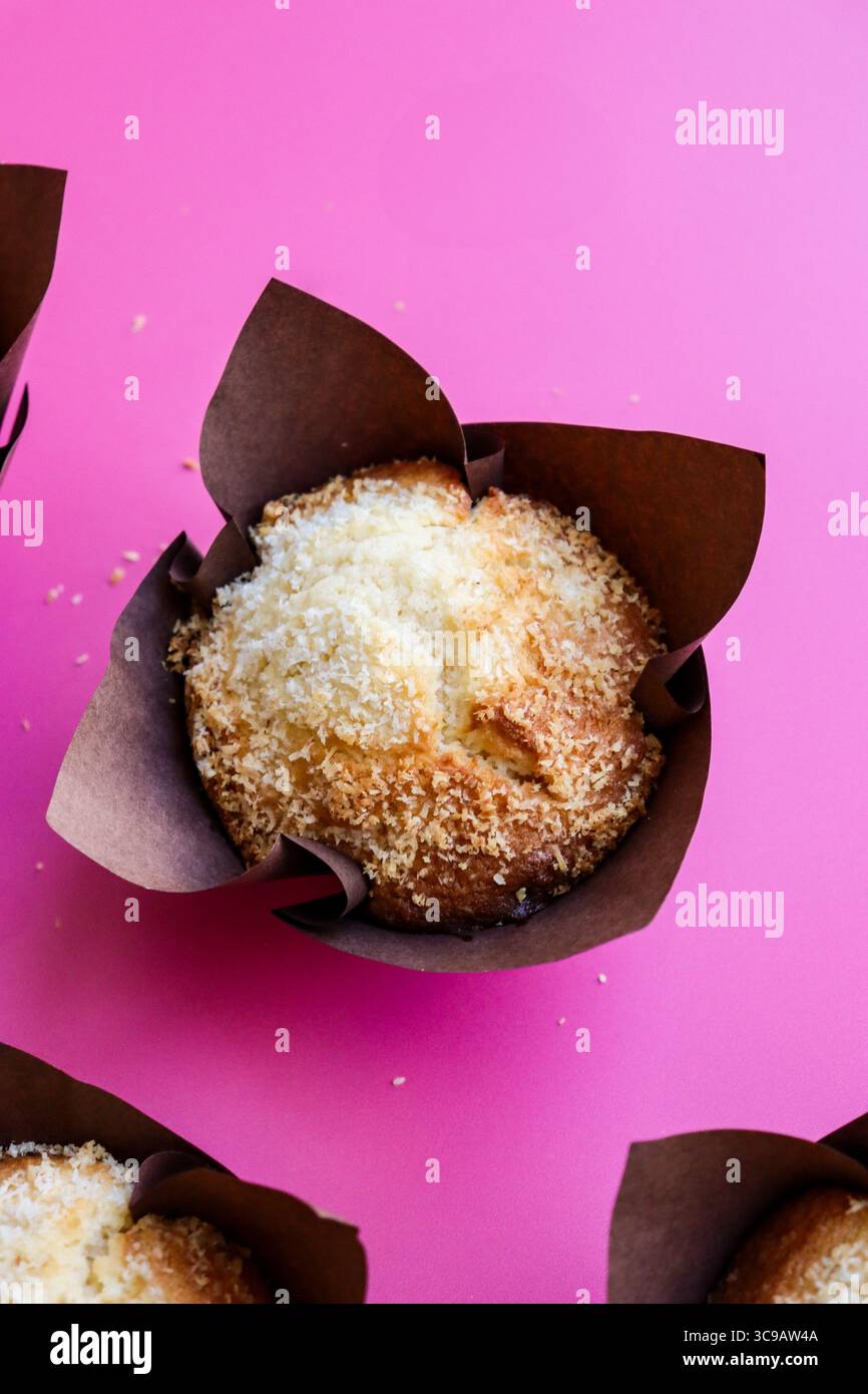Eine Nahaufnahme eines frisch gebackenen Muffins in einem braunen Tulpen-ähnlichen Papierbecher vor einem leuchtend rosa Hintergrund. Der Muffin ist goldbraun Stockfoto