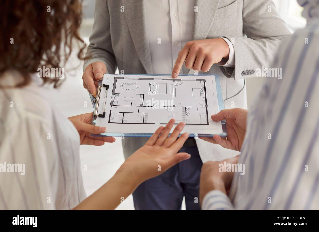 Immobilienmakler zeigt einem jungen Paar einen Wohnungsplan und bespricht das Layout der Wohnung während der Beratung Stockfoto