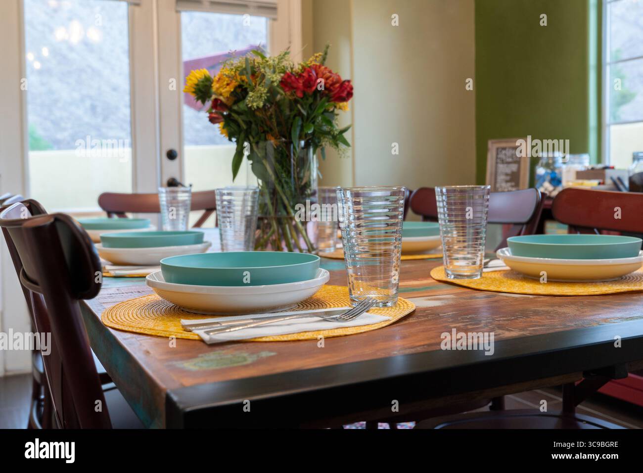 Esstisch mit Stühlen, Set mit frischen Blumen in Vase Teller Schüsseln Besteck und Trinkgläser. Niedrige Ansicht Stockfoto