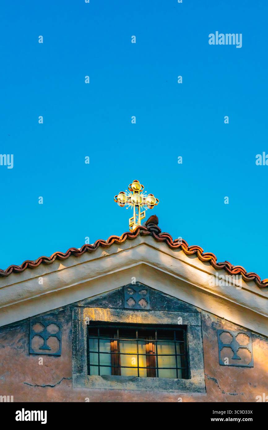 Ein goldenes Kreuz steht auf der Kuppel einer orthodoxen Kirche mit einem Glockenturm, von unten gesehen unter einem dramatischen bewölkten Himmel in einem spirituellen und historischen Set Stockfoto
