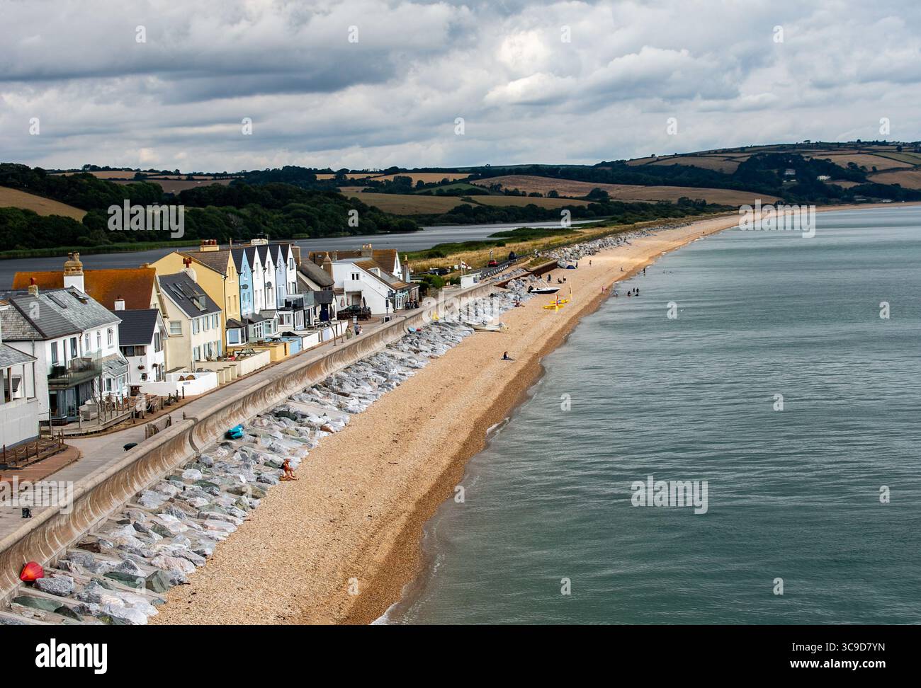 Das malerische Küstendorf Slapton Sands mit einem langen Kieselstrand, gesäumt von bunten Häusern und ruhigem Wasser unter einem bewölkten Himmel Stockfoto