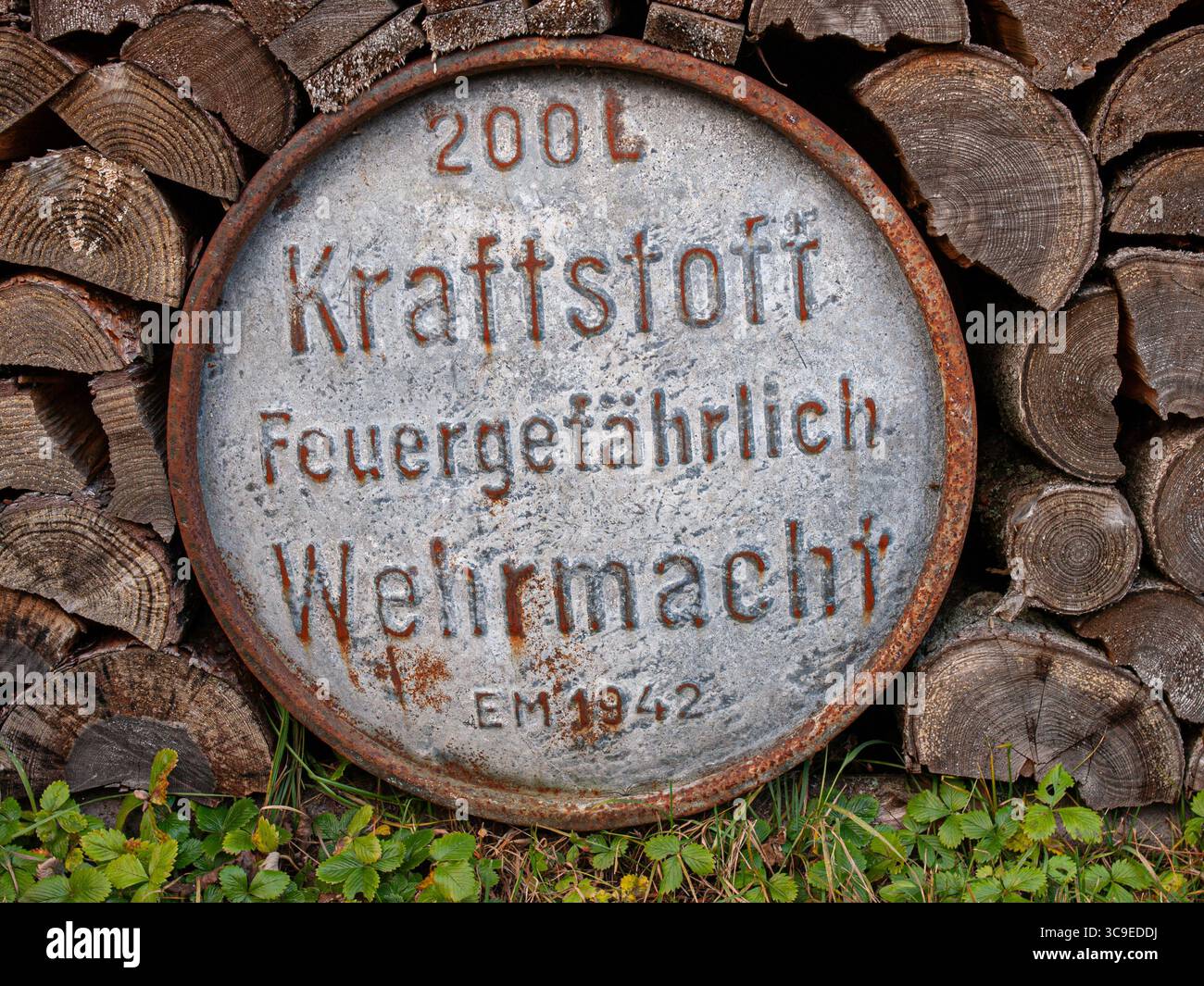 Die ursprüngliche Wehrmacht-Brennstofftrommel aus dem 2. Weltkrieg ist teilweise hinter einem Holzstapel im ländlichen Estland versteckt, mit deutschem Text und rostiger Metalloberfläche Stockfoto
