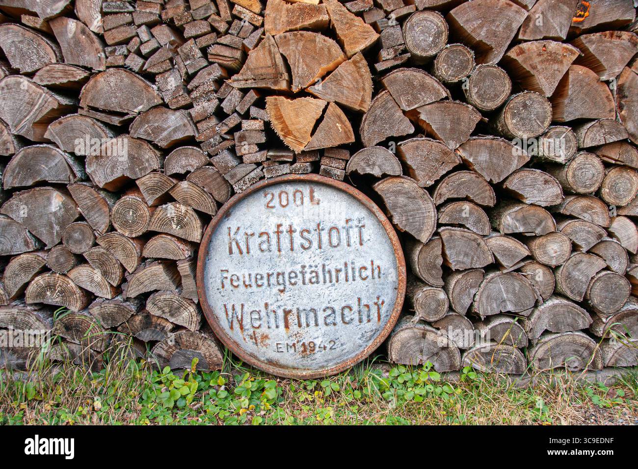 Die ursprüngliche Wehrmacht-Brennstofftrommel aus dem 2. Weltkrieg ist teilweise hinter einem Holzstapel im ländlichen Estland versteckt, mit deutschem Text und rostiger Metalloberfläche Stockfoto