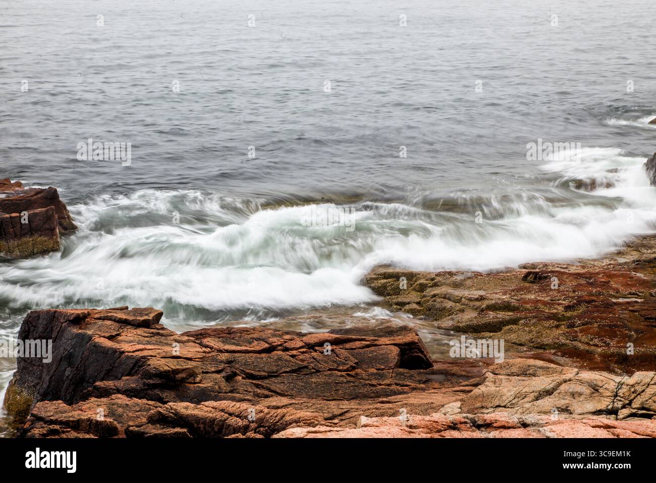 Wellen krachen bei Sonnenaufgang sanft gegen die zerklüfteten Felsen entlang der Küste und schaffen eine ruhige Atmosphäre. Das sanfte Licht reflektiert das Wasser und verbessert so die Qualität Stockfoto