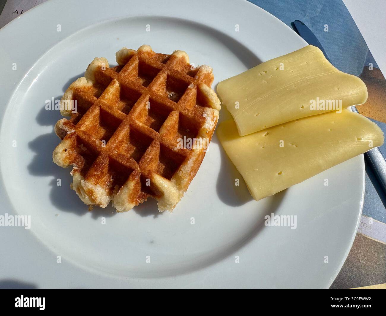 Goldene Waffel, serviert mit zwei Scheiben Gelbkäse auf einem weißen Teller. Stockfoto