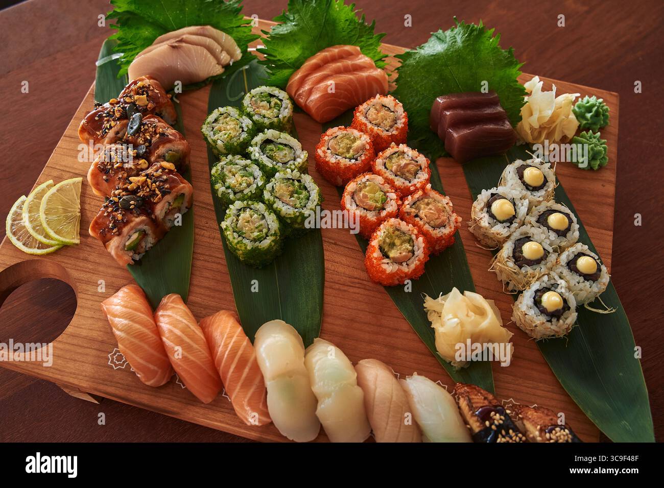Eine lebendige Sushi-Platte mit einer Auswahl an frischen Gerichten, darunter Rolls, Sashimi und bunte Pflaster auf einem Holzbrett Stockfoto