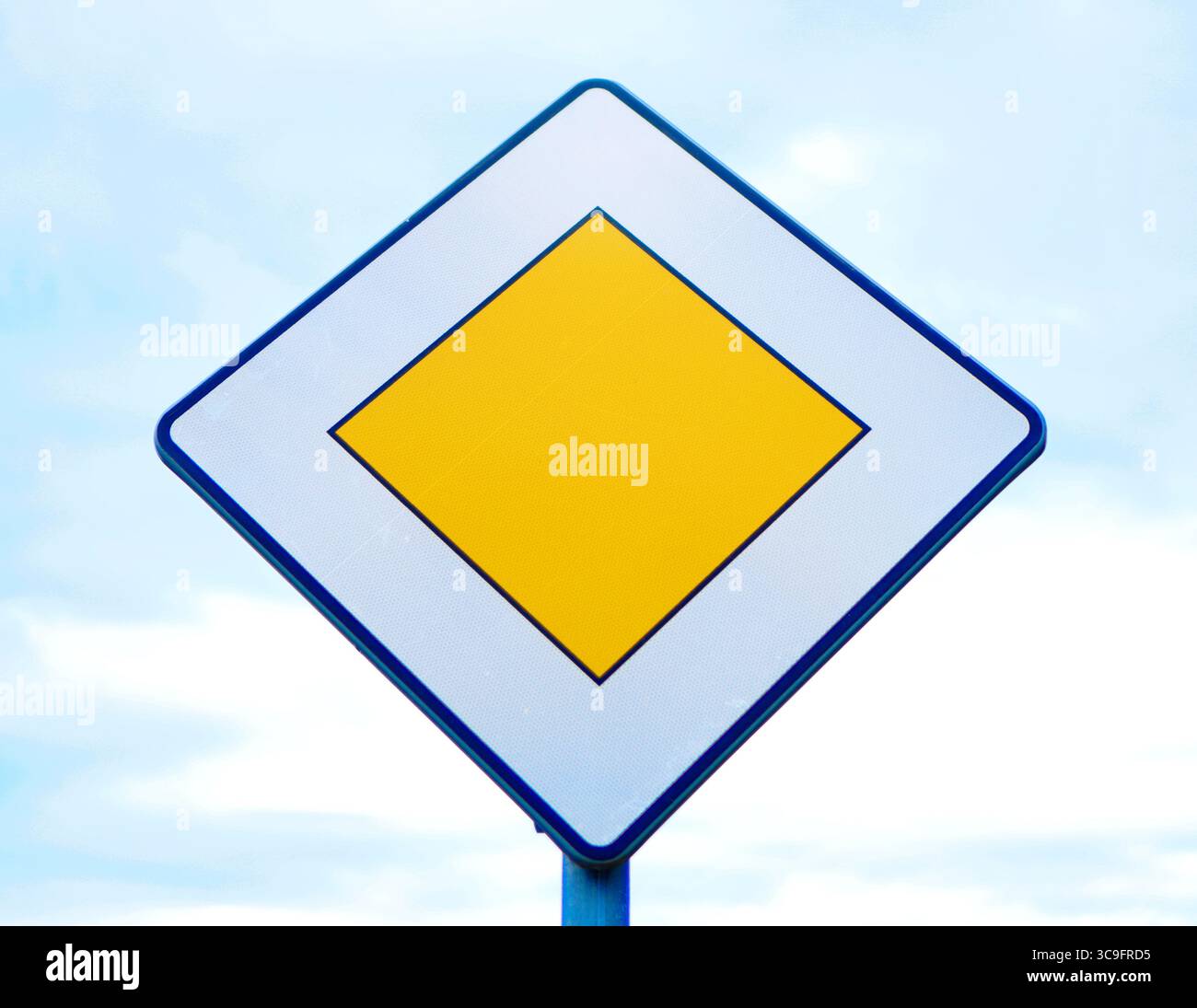 Gelbes, diamantbesetztes Verkehrsschild an einem Pfosten, das die vorrangige Straße vor Ihnen anzeigt. Stockfoto