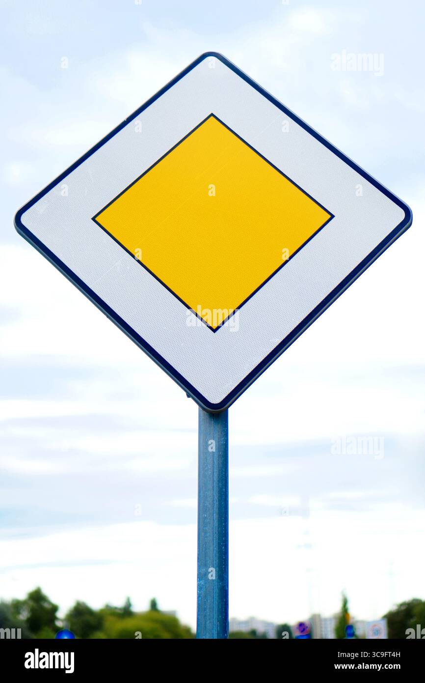 Gelbes, diamantbesetztes Verkehrsschild an einem Pfosten, das die vorrangige Straße vor Ihnen anzeigt. Stockfoto