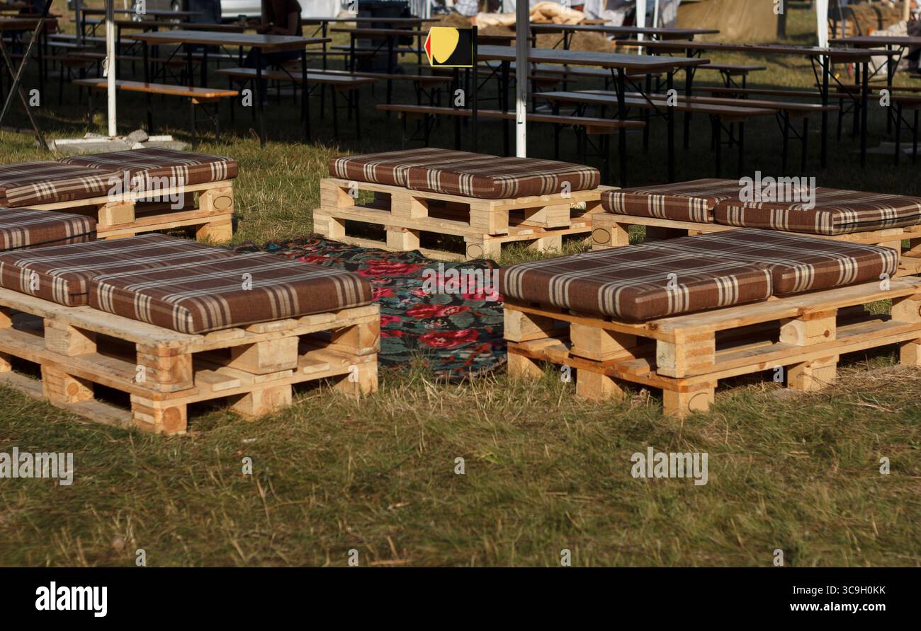 Holzpaletten, die als Sitzplatz mit gestreiften Kissen auf einem grasbewachsenen Bereich angeordnet sind. Ideal für Versammlungen im Freien oder Veranstaltungen Stockfoto