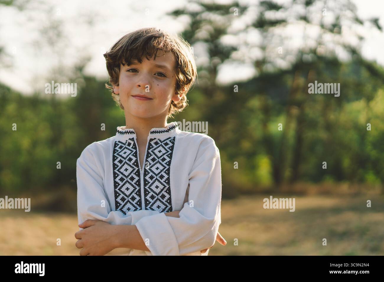 Ein Junge lächelt selbstbewusst, während er auf einem sonnendurchfluteten Feld steht und ein traditionelles besticktes Hemd trägt Stockfoto