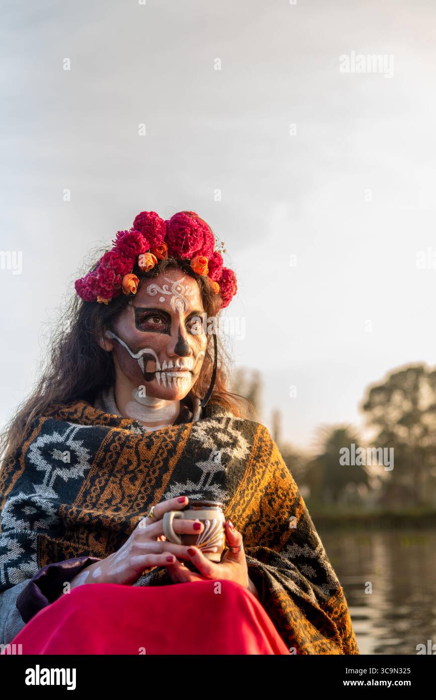 Eine Frau, die als La Catrina charakterisiert ist, auf einem Trajinera-Boot während des Sonnenaufgangs in den Kanälen von Xochimilco, Mexiko. Stockfoto